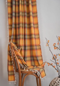 Detail of orange plaid fabric curtain featuring white tassel trim and thick texture