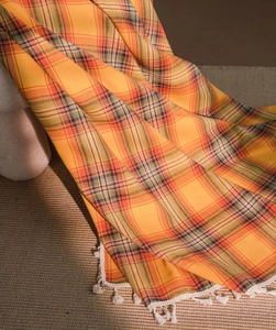 Close-up detail of warm orange plaid fabric with soft texture and white fringe tassels