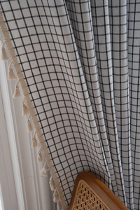 Close-up of black and white checkered fabric with cream tassel trim and linen texture