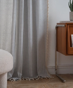 Detail of black and white grid curtains with handmade beige tassels in a cozy home setting