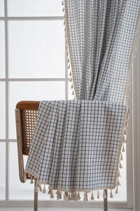 Detail of black and white plaid curtain fabric with cream tassels on a wooden chair