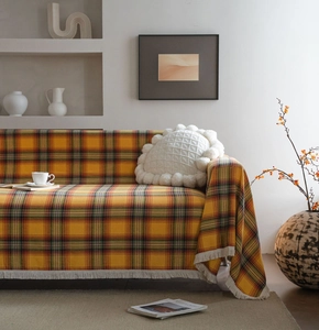 Dettaglio coperta scozzese gialla con trama a maglia spessa e nappe bianche decorative