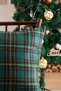 Close-up of green Scottish tartan pillowcase leaning on a wooden chair with Christmas tree