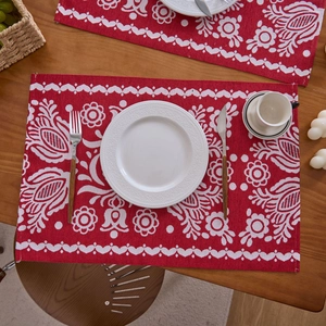 Detailansicht eines roten Jacquard-Tischsets mit Blumenmustern auf einem Holztisch