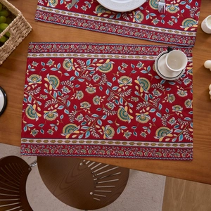 Detailaufnahme eines roten Jacquard-Platzsets mit Blumenmuster auf einem rustikalen Holztisch