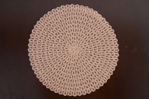 Detailed top view of a pink woven circular placemat with fringe on a dark wood table