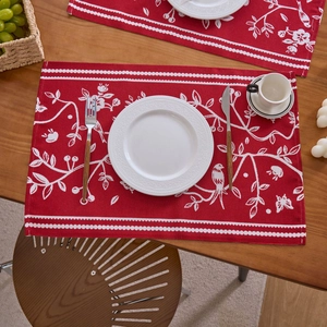 Detailansicht roter Jacquard-Tischsets mit Blumenmustern und Vögeln auf einem Esstisch aus Holz