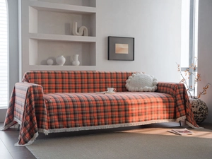 Close-up of rust red plaid sofa cover with elegant white tassels in minimalist setting
