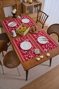 Detailansicht von vier roten Jacquard-Tischsets mit Blumenmuster auf einem Holztisch