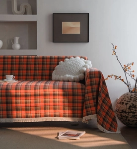 Detail of rust red plaid sofa cover showing woven fabric texture and white fringe edges