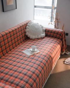 Detail view of rustic orange and brown plaid sofa cover with elegant white tassels