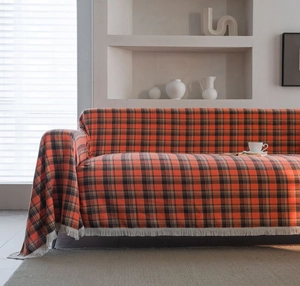 Detail of rust red plaid sofa cover with white fringe on a minimalist couch