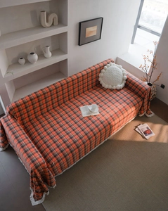 Detailed view of rust red plaid sofa cover with white fringe and thick woven texture