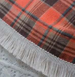 Detailed close-up of rusty red plaid fabric with fine weave texture and cream tassels