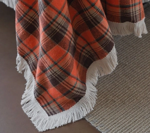 Close-up of rust red plaid fabric with elegant cream fringe tassels and soft texture