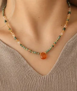 Close-up of beaded necklace with orange teardrop stone pendant on beige knit sweater