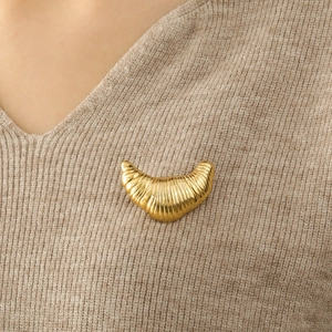 Detailed view of a gold croissant brooch on a beige knit sweater showcasing metallic luster