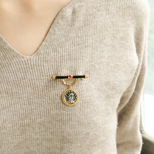 Vintage relief coin brooch with red gemstone and black enamel detail on knitwear