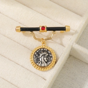 Vintage relief coin brooch with black enamel bar and red gemstone on a jewelry box