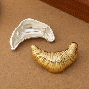 Polished gold croissant brooch with detailed bread texture and silver pin backing