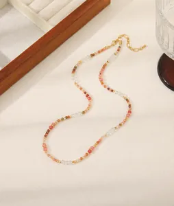 Detalle de collar de cuentas con cristales rosas, naranjas y dorados sobre tela