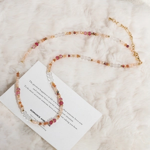 Collar de cuentas de colores con cristales rosa y cierre dorado sobre fondo de piel sintética blanca
