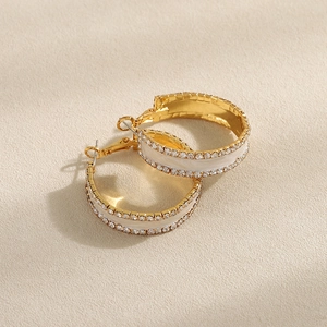 Detalle de pendientes de aro dorados con incrustación de esmalte blanco y filas de circonitas