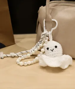 Detail of handmade crochet ghost charm with pearl bead chain hanging on a leather bag