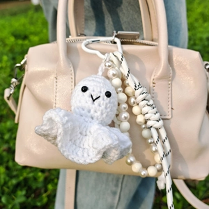 Handmade white crochet ghost charm with pearl beads and heart carabiner on a bag