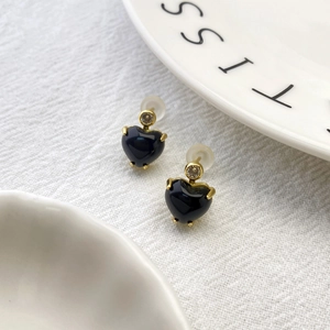 Detail of black heart earrings with gold base and clear zircon accents on white fabric