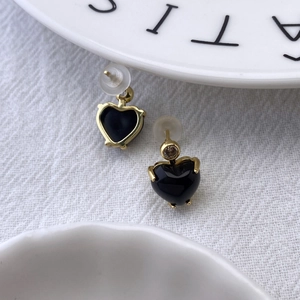 Detailed close-up of golden heart-shaped earrings with black inlay on white fabric
