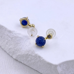 Macro shot of gold stud earrings featuring a blue lapis lazuli stone and clear zircon
