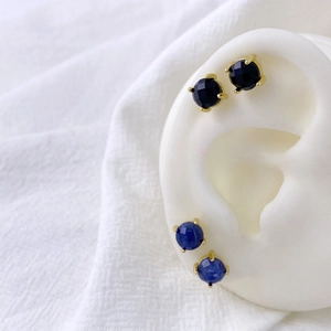 Close-up of gold-plated stud earrings with circular blue and black zircon stones on ear model