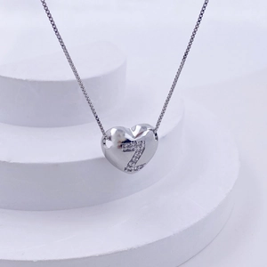 Macro detail of silver heart necklace with crystal letter Z on minimalist white stand