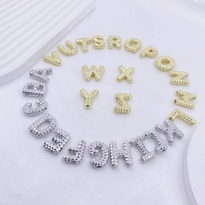 Makroansicht goldener und silberner Buchstabenanhänger mit strukturierter Perloberfläche