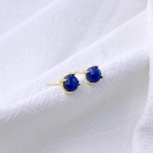 Detailed view of round blue zircon earrings with gold four-prong setting on white fabric