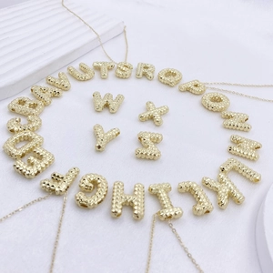 Detailansicht von 26 goldenen Buchstabenanhängern mit geprägten 3D-Reliefstrukturen