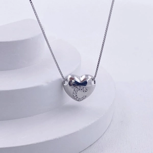 Macro shot of silver heart pendant with letter C on white tiered display stand