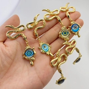 Detail of hand holding gold snake evil eye earrings with textured blue enamel pendants