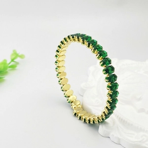 Détail macro d'un bracelet doré orné d'une rangée de zircons verts à taille ovale