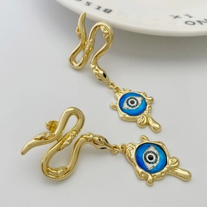 Macro detail of gold snake stud earrings with blue evil eye pendants on grey background