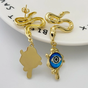 Macro shot of gold snake-shaped earrings with a blue evil eye pendant detail