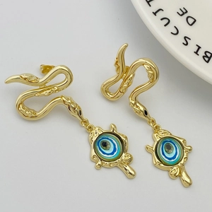 Detailed close-up of golden snake stud earrings with blue evil eye charms on white plate