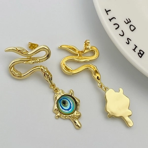 Detail of gold snake earrings with evil eye charm on a white ceramic plate background