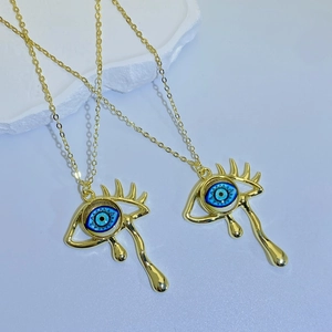 Macro detail of teary evil eye pendant necklace with blue pupil and golden eyelashes