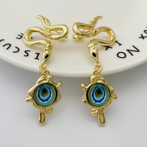 Golden snake stud earrings with multi-colored evil eye pendant on a white ceramic plate