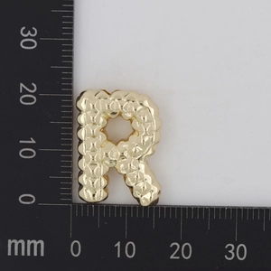 Makroaufnahme des goldener Buchstaben R Anhänger mit Steppmuster und Skalamessung