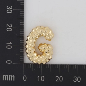 Makroaufnahme eines gehämmerten goldenen G-Anhängers neben einer Skala mit 25 mm Höhe