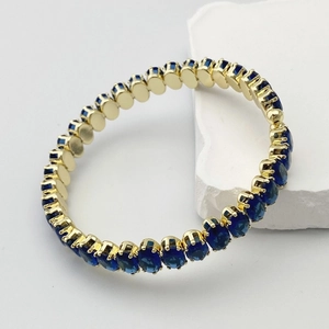 Détail d'un bracelet de tennis doré orné de zircons ovales bleu foncé sertis à griffes