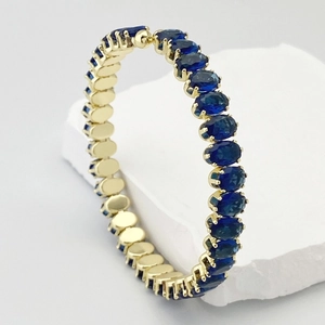 Détail d'un bracelet doré avec des zircons bleus à coupe ovale et sertissage à quatre griffes